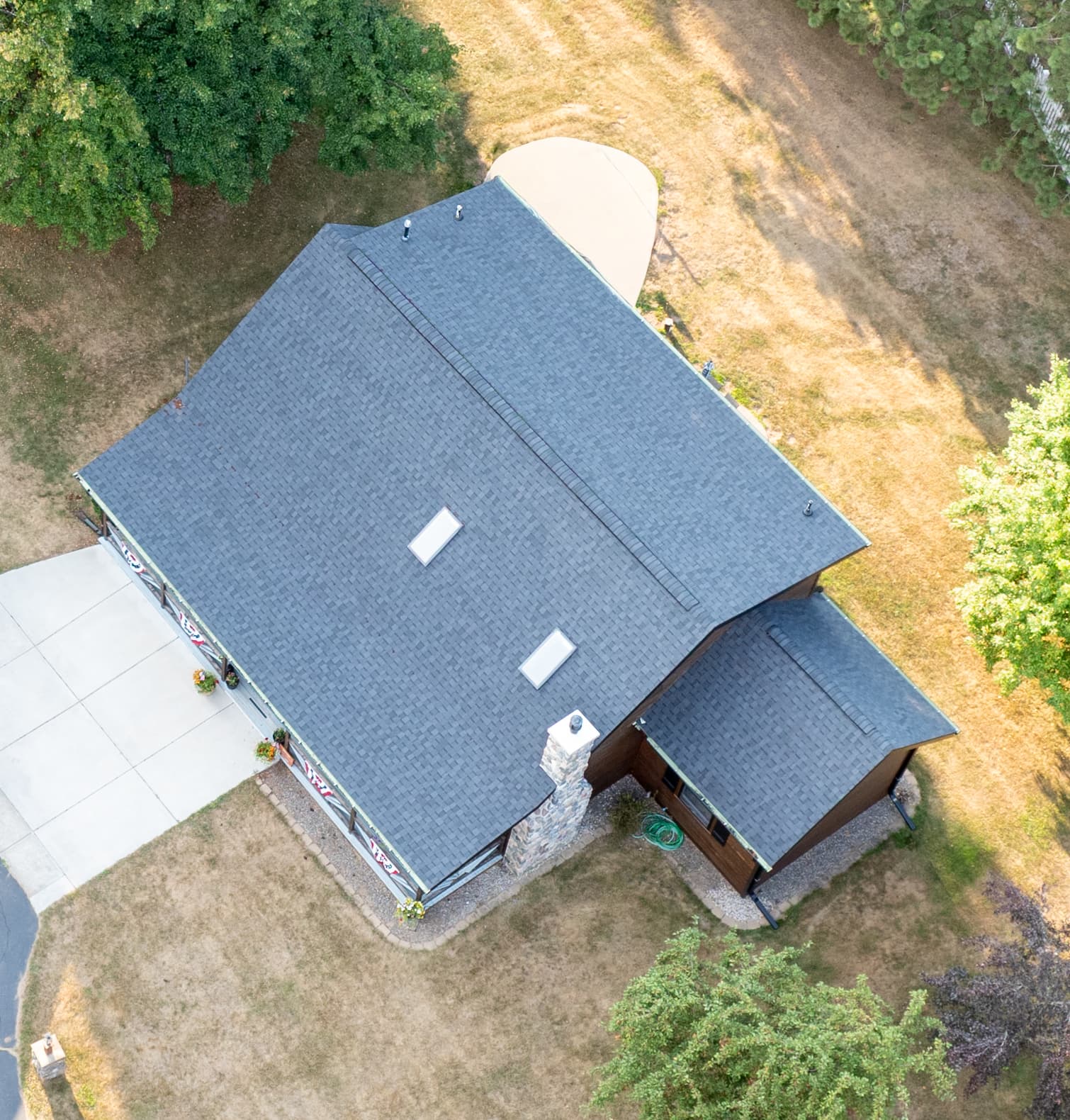 Aerial view of a shingle roof and matching covered entry on a wooded Wisconsin property