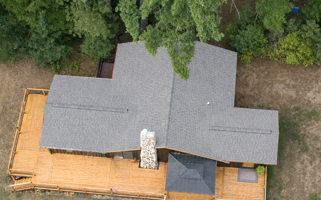 Overhead aerial view of a completed cabin roof with stone chimney and wraparound deck